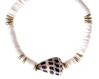 May include: A stretch bracelet featuring white disc-shaped beads, metallic gold-toned spacer beads, and a single cone-shaped seashell with a brown and white checkered pattern. The beads are arranged in a circular pattern with the shell as a focal point.