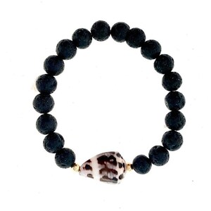 May include: A black lava rock beaded bracelet with a white and brown seashell charm.
