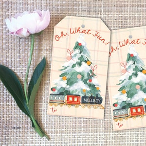 May include: Two Christmas gift tags with a watercolor illustration of a snowy Christmas tree and a train. The tags have the text "Oh, What Fun!" in red and a space to write "To:". The background is a beige plaid.