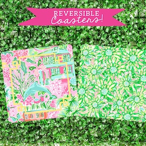 May include: Two reversible coasters. One side features a pink and green floral pattern with a dolphin and a house. The other side features a green and pink floral pattern. The coasters say "REVERSIBLE Coasters!"