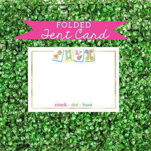 May include: A folded card with a pink banner that says "FOLDED Jent Card". The card has a white background with a gold border and a row of colorful tiles with flowers and letters. The text "crack dot bam" is printed in blue and pink at the bottom of the card.
