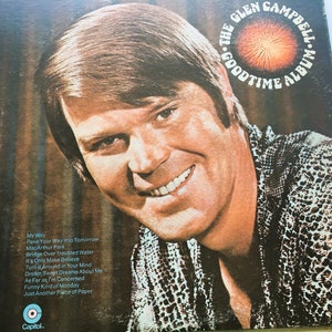 May include: A vintage vinyl record album cover featuring a smiling man with brown hair. The album is titled "The Glen Campbell Goodtime Album" with a red sunburst design. The album cover is a brown and black snake skin pattern.