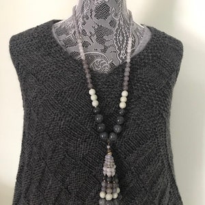 May include: A gray, white, and black beaded necklace with a tassel pendant. The necklace is on a gray sweater.