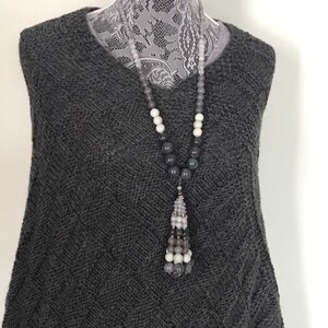 May include: A gray knitted sweater with a long gray, white, and light pink beaded necklace with a tassel.
