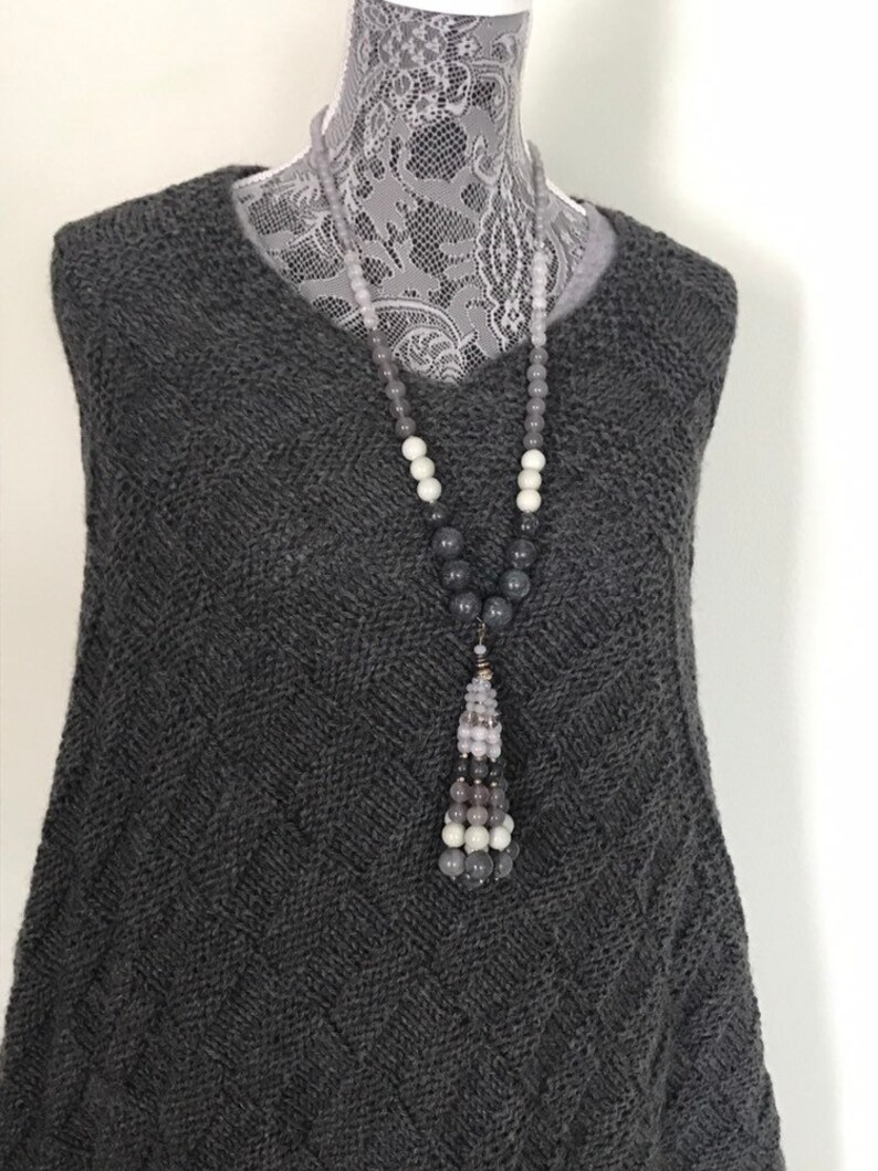 May include: A gray knitted sweater with a long gray, white, and light pink beaded necklace with a tassel.