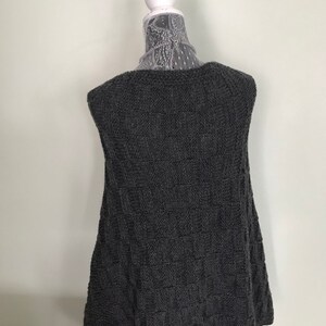 May include: A sleeveless gray knitted vest with a textured pattern. The vest is displayed on a white mannequin.