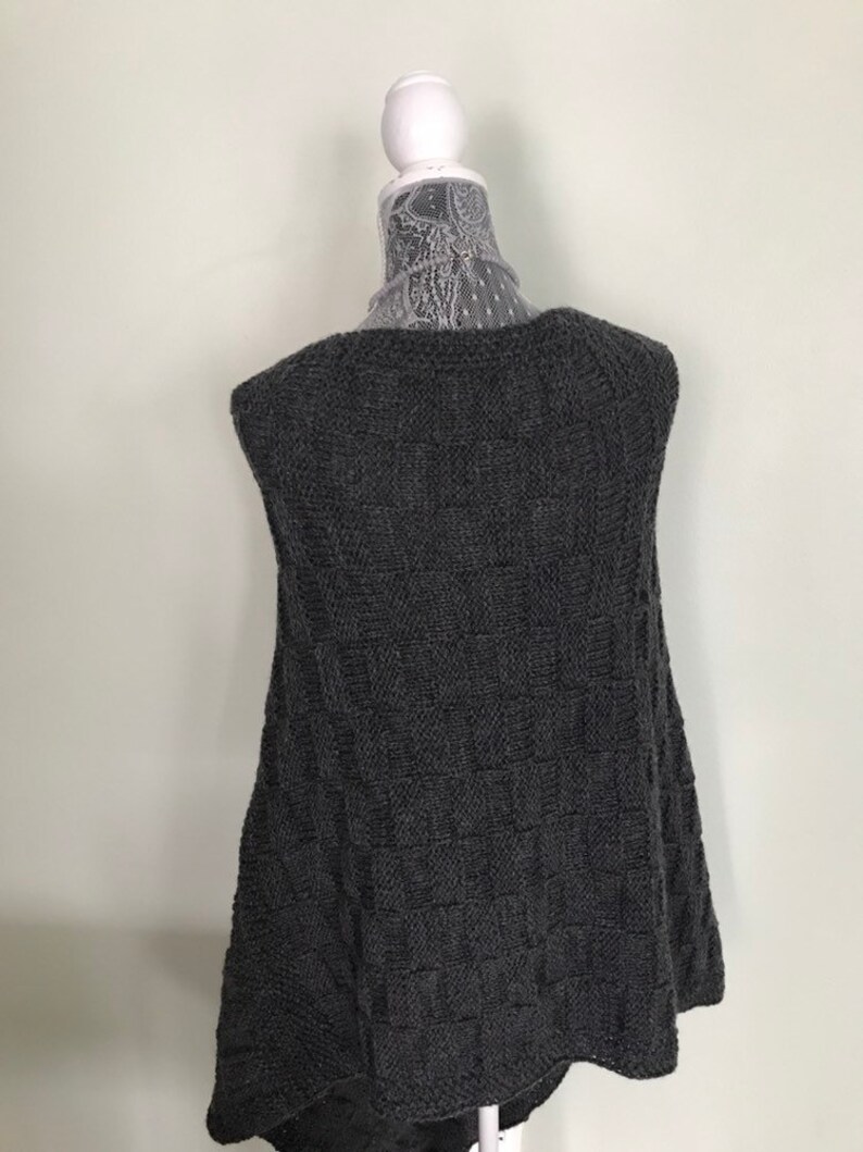 May include: A sleeveless gray knitted vest with a textured pattern. The vest is displayed on a white mannequin.