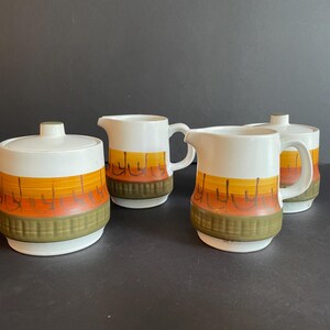 May include: A set of four vintage ceramic creamer and sugar bowls with a brown, orange, and yellow geometric pattern.
