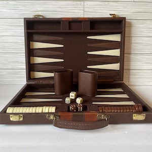 May include: Open brown backgammon set with ivory and brown game pieces, dice, and leather dice cups. The game board is brown with ivory and brown triangles. The set is in a brown case with a leather handle and gold-colored hardware.