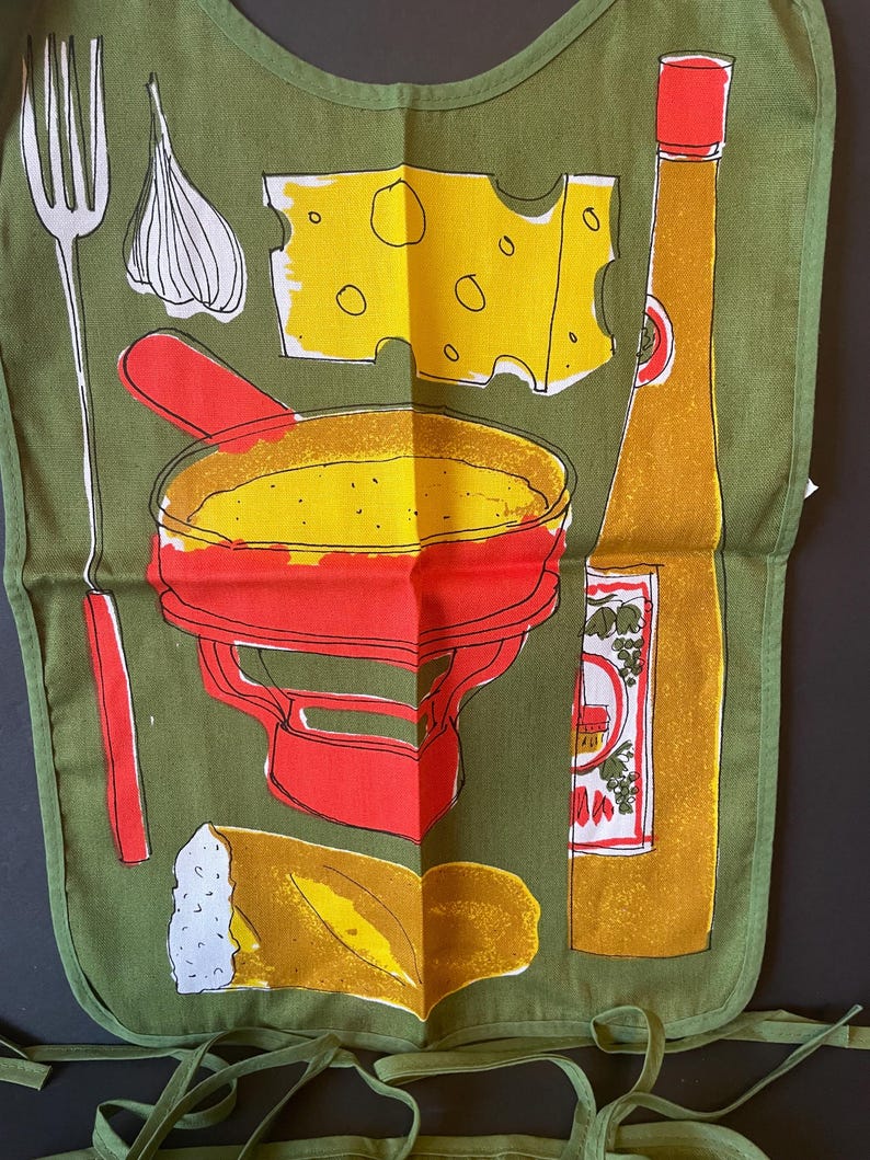 May include: An olive green apron featuring a graphic print of a red fondue pot, a yellow block of Swiss cheese, a long fork, a clove of garlic, a piece of crusty bread, and a tall yellow bottle with a red cap, all outlined in black ink.
