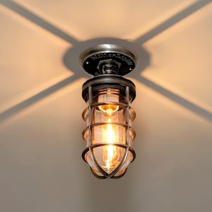 May include: A silver caged ceiling light fixture with a clear glass shade and a single light bulb turned on.