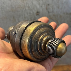 May include: A vintage brass and metal object with a cylindrical shape, featuring a series of concentric rings and a rounded end. The object has a tarnished, aged appearance, suggesting it is an antique or a piece of industrial design.