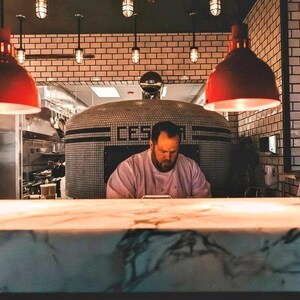 A row of vintage industrial pendant lights with metal cages and glowing bulbs, hanging above a bustling restaurant kitchen