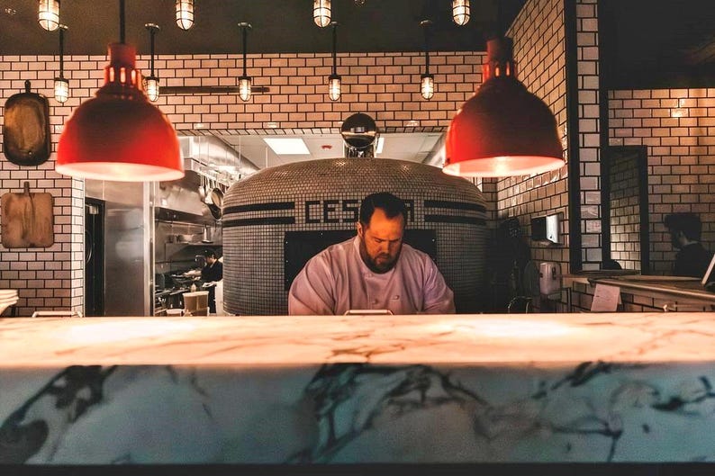A row of vintage industrial pendant lights with metal cages and glowing bulbs, hanging above a bustling restaurant kitchen