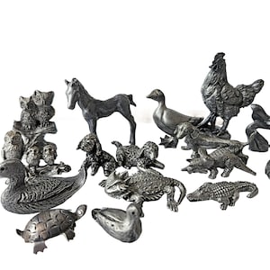 May include: A collection of small, metallic-toned animal figurines including a horse, a rooster, a duck, a turtle, a lizard, a crocodile, and various dogs and owls. Each piece features detailed textures and a uniform silver-gray finish.