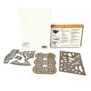 May include: A Cuttlebug Halloween Holiday die-cutting set including a white storage box, an instruction sheet, and metal cutting dies featuring an owl, a bat, a spider web, and six jack-o'-lantern pumpkins on white backing sheets.