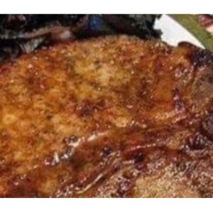 May include: A close-up of a cooked pork chop with a crispy brown exterior. The chop is sitting on a plate with a side of cooked vegetables.