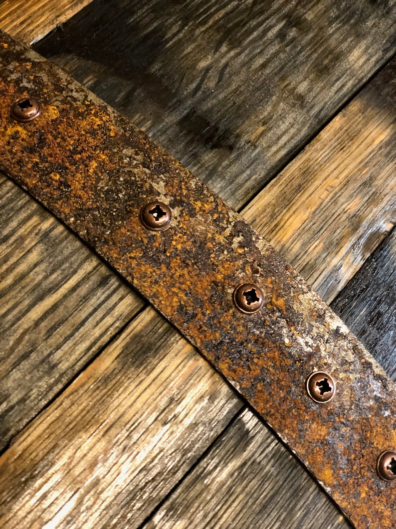 May include: A close-up of a rustic wooden surface with a rusty metal band. The band is secured with several copper screws. The wood has a natural grain pattern and is stained a dark brown color.
