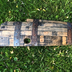 May include: A wooden barrel stave with metal bands and a hole in the center. The stave is stained dark brown and has a rustic appearance.