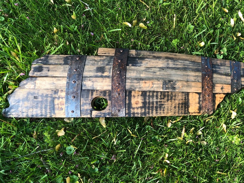May include: A wooden barrel stave with metal bands and a hole in the center. The stave is stained dark brown and has a rustic appearance.
