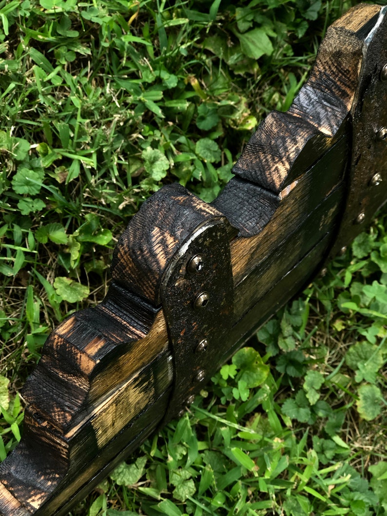 May include: A wooden wall decor piece with a black and brown finish. The piece is shaped like a series of overlapping arches and has metal accents.