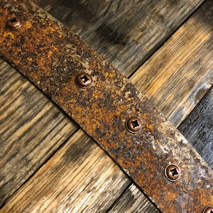 May include: A close-up of a rustic wooden surface with a rusty metal band. The band is secured with several copper screws. The wood has a natural grain pattern and is stained a dark brown color.