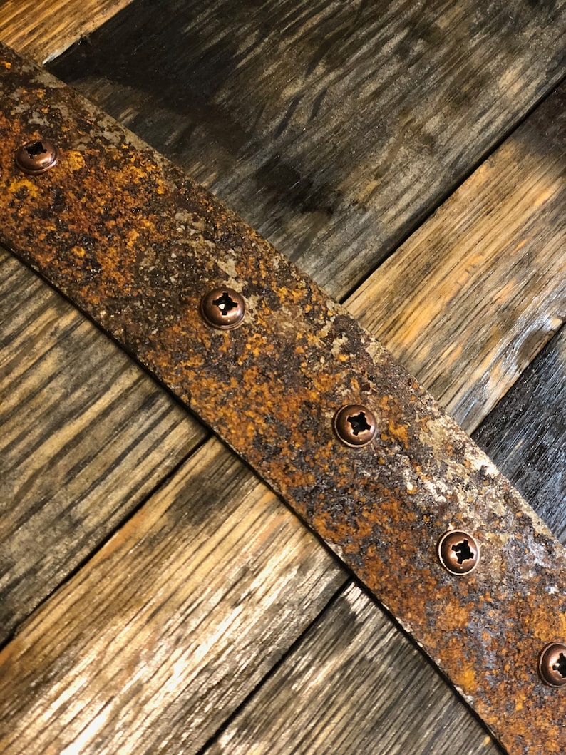 May include: A close-up of a rustic wooden surface with a rusty metal band. The band is secured with several copper screws. The wood has a natural grain pattern and is stained a dark brown color.