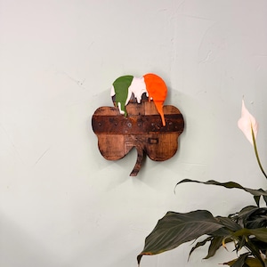 May include: A wooden shamrock with a green, white and orange paint design. The paint is dripping down the shamrock.