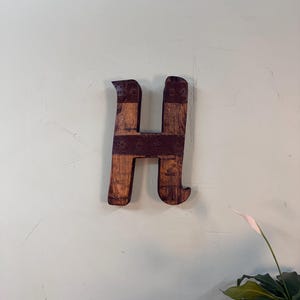 Puede incluir: Un letrero de madera rústico con el texto "Welcome to our home" en un estilo manuscrito. El letrero presenta un acabado envejecido y un diseño simple y acogedor, perfecto para un porche o entrada.