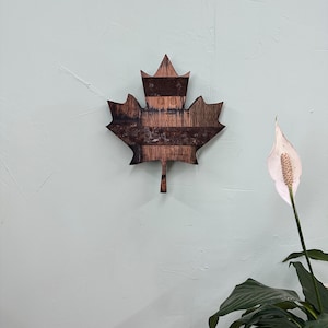 Puede incluir: Una decoración de pared de hoja de arce de madera hecha de madera recuperada con un acabado marrón rústico.