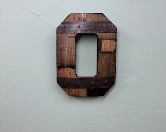 May include: A wooden letter O, crafted from reclaimed wood and accented with metal bands. The letter is painted a dark brown color and has a rustic, industrial look.