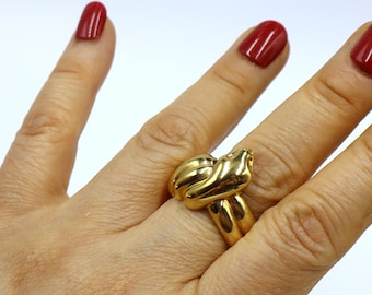 Könnte beinhalten: Ein goldener Knotenring mit einem dicken Band. Der Ring wird an einem Finger mit rotem Nagellack getragen.