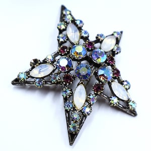 May include: A silver star-shaped brooch with iridescent blue, purple, and clear rhinestones and white opaque stones.