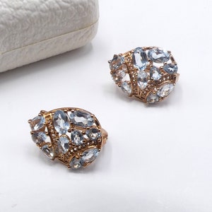 May include: A pair of gold earrings with a cluster of light blue gemstones. The earrings are shaped like a teardrop and have a delicate design.