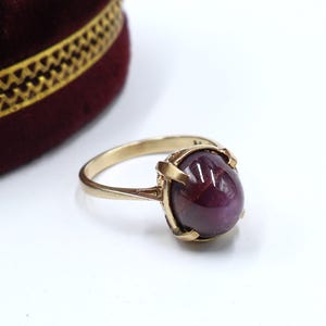 May include: A gold ring with a large, oval-shaped, dark red gemstone set in a claw setting.