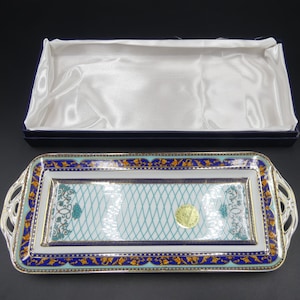 May include: A rectangular serving tray with ornate gold and blue trim. The tray has a white background with a turquoise and white lattice design. The tray has two handles on the sides.