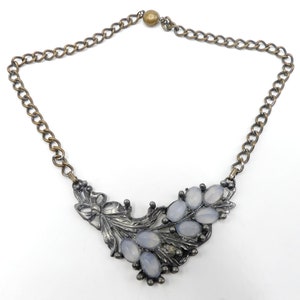May include: A silver tone necklace with a floral design and light blue glass stones. The necklace has a brass chain.