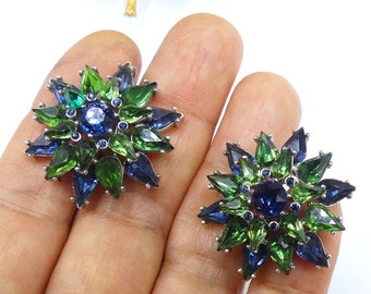 May include: A pair of vintage earrings with a green and blue starburst design. The earrings are made of metal and have a cluster of rhinestones in the center.