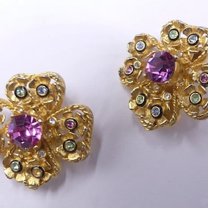 May include: A pair of gold tone flower-shaped earrings with pink, green, and clear rhinestones.