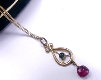 May include: A gold pendant necklace with a green gemstone and a dangling red gemstone. The pendant is shaped like a teardrop with a delicate design.