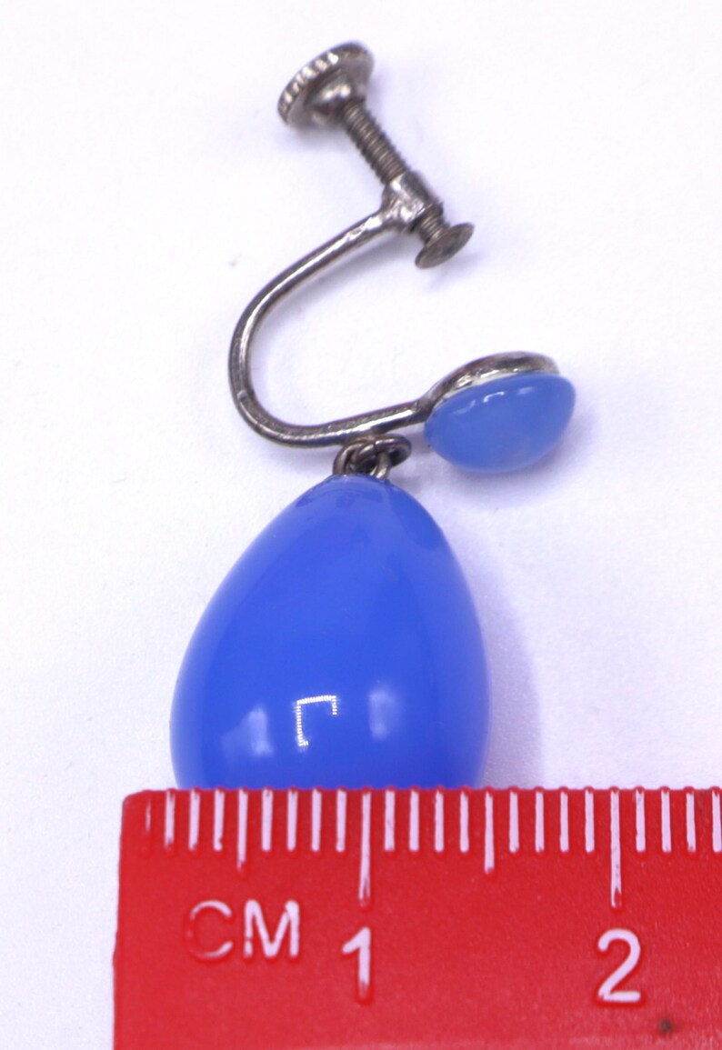 K&ouml;nnte beinhalten: Vintage Ohrring mit Schraubverschluss und einem tropfenf&ouml;rmigen, hellblauen Stein. Die Metallteile des Ohrrings sind silberfarben. Der Stein misst etwa 1 cm in der L&auml;nge. Auf wei&szlig;em Hintergrund.