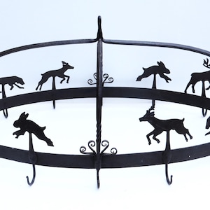 May include: Black metal pot rack featuring silhouettes of various animals, including deer, rabbits, and dogs. The rack has a circular design with hooks for hanging pots and pans. Decorative and functional kitchen decor.