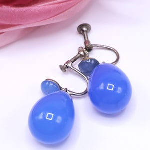K&ouml;nnte beinhalten: Vintage blaue Tropfenohrringe mit silberfarbenen Metallbeschl&auml;gen. Die Ohrringe haben einen Schraubverschluss und eine gl&auml;nzende Oberfl&auml;che. Die Tropfenform ist ein klassisches Design, und die blaue Farbe sorgt f&uuml;r einen Farbtupfer.