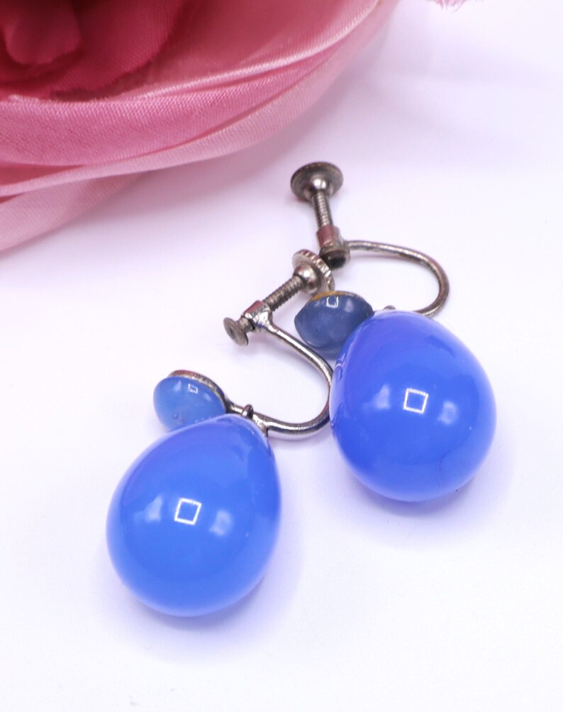 K&ouml;nnte beinhalten: Vintage blaue Tropfenohrringe mit silberfarbenen Metallbeschl&auml;gen. Die Ohrringe haben einen Schraubverschluss und eine gl&auml;nzende Oberfl&auml;che. Die Tropfenform ist ein klassisches Design, und die blaue Farbe sorgt f&uuml;r einen Farbtupfer.
