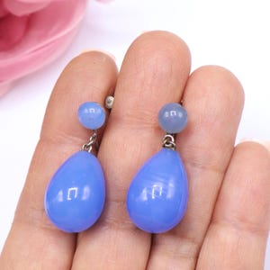 K&ouml;nnte beinhalten: Ein Paar blaue Vintage-Ohrringe. Jeder Ohrring hat eine kleine, runde Perle oben und eine gr&ouml;&szlig;ere, tropfenf&ouml;rmige Perle unten, verbunden durch silberfarbenes Metall. Die Ohrringe werden in einer Hand gehalten.