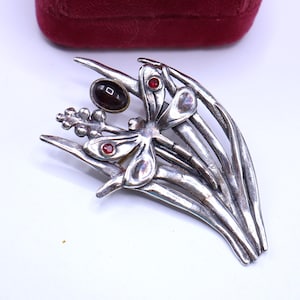 May include: Silver-toned dragonfly brooch with red and brown accents. The brooch features a dragonfly design with red gemstone eyes and a brown gemstone head. The brooch is set against a white background and a red velvet box.