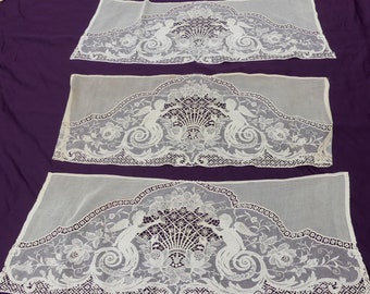 May include: Three white lace valances with a delicate floral and angel design. The valances are made of a sheer fabric and have a scalloped edge.