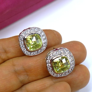 May include: A pair of silver earrings with a large, square, light green gemstone surrounded by a halo of smaller, clear gemstones.