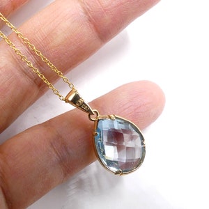 May include: A gold chain necklace with a teardrop-shaped pendant featuring a clear blue gemstone.
