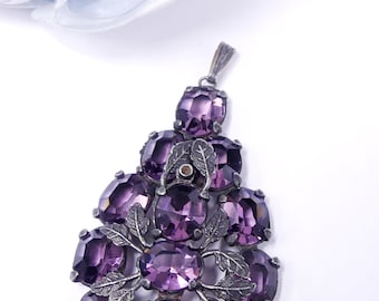 May include: A silver pendant featuring a cluster of purple faceted glass stones set in a floral design.